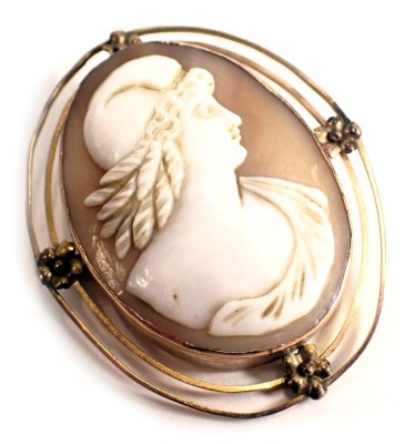 A shell cameo brooch, the oval cameo depicting maiden with helmet, in a two row outer wire border with floral cluster group, yellow metal with rubbed marks, on single pin back with safety chain, 5cm x 4cm, 9.7g all in.