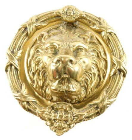 A large brass lion mask door knocker, with circular wreath decorated with flower heads, ribbons, etc., 22cm diameter.