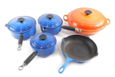 A large orange enamel Le Creuset circular pan, and other blue enamel Le Creuset pans.