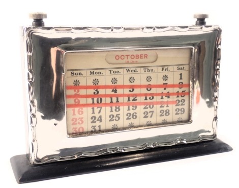 A George V silver cased and ebonised desk calendar, the silvered frame with waved border, in a black painted ebonised case, with two turn handle, Birmingham 1931, 13cm high, 21cm wide, 4cm deep.