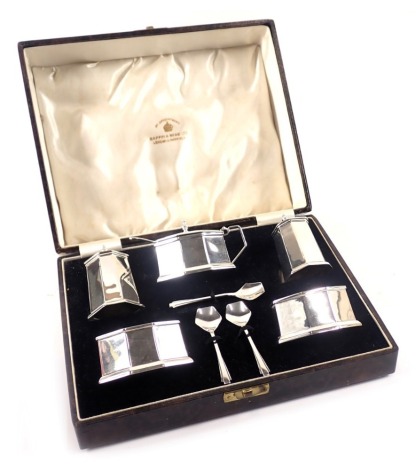 A Mappin and Webb silver Art Deco cruet set, comprising salt and pepper, two preserve bowls, and a preserve jar with lid, each with blue glass liner, including three shell capped spoons and an associated spoon, 6.49oz gross, in fitted case.