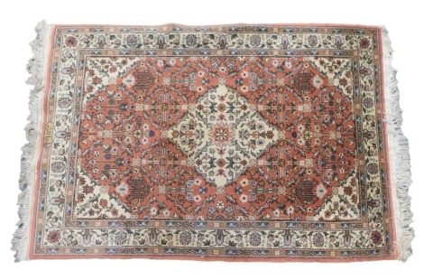 A Persian style rug, with a central cream patterned lozenge, on an orange ground with cream spandrels, one wide and two narrow borders, signed to border, 150cm x 106cm.