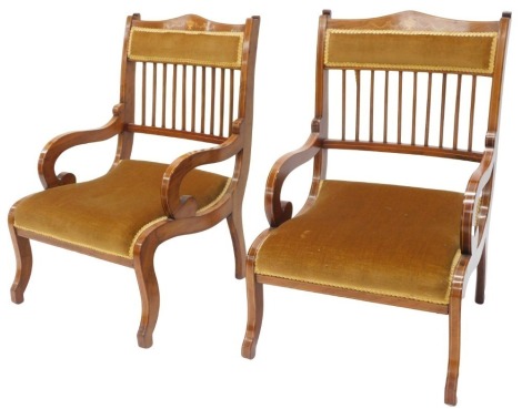 A pair of Edwardian mahogany and marquetry low chairs or nursing chairs, each with a padded back and seat, scrolling arms, on sabre legs.