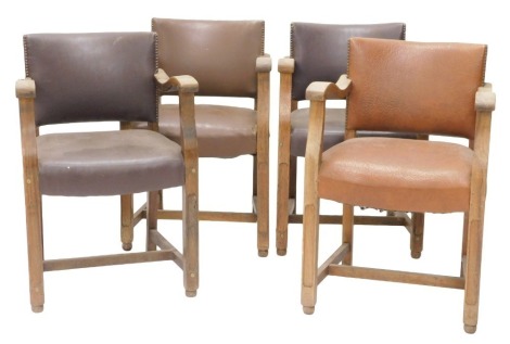 A set of four early 20thC oak open armchairs, each with a brown leatherette padded seat, within studded borders.