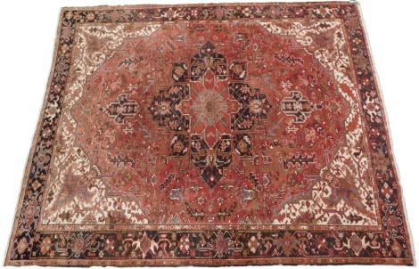 A Heriz Persian carpet, with a design of medallions, scrolls, etc., in mainly red on a cream ground, one wide and two narrow borders, 348 x 288 cm.