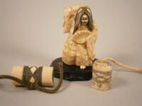 A Japanese ivory netsuke carved in the form of a grotesque female figure and two bone carvings on a