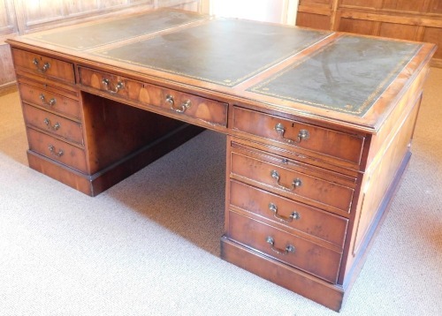 A 20thC yew partner's desk, the top with three green gilt tooled leather insets, with a moulded edge, with an arrangement of four drawers, sliding shallow drawer and two faux drawer cupboards to each side, on a plinth base, 75cm high, 180cm wide, 127cm de