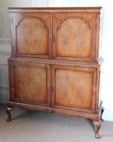 A Queen Anne style walnut cocktail cabinet, the top with a moulded edge above two hinged doors enclosing a shaped shelf picked out in gilt with green interior and sliding drawer, the base with two cupboards enclosing a shelf to each top, on shell carved l