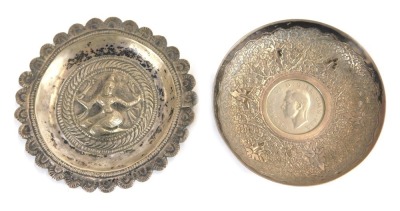 An Indian white metal trinket dish, of circular form engraved with leaf motif decoration, inset centrally with a George VI 1951 two shilling coin, 7.5cm diameter, together with an Eastern white metal trinket dish of circular form with petalated border, em