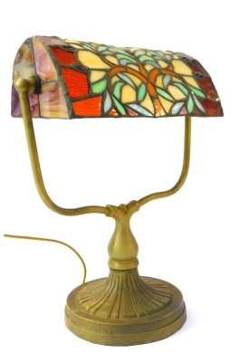 A Tiffany style desk lamp, the leaded glass shade decorated with a tree raised on a cast metal base on circular foot, 35cm high.