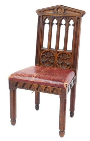 A Victorian oak chair in the Gothic style, the back with four pierced sections, above two floral motifs, with an overstuffed seat, the front and side apron decorated with carved Gothic motifs raised on chamfered legs.