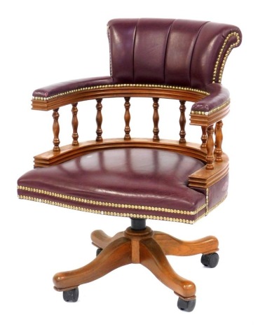 A 20thC burgundy leather oak framed captain's chair, with overstuffed leather back and seat, with brass stud work, united by turned oak columns, on castors, 86cm high.