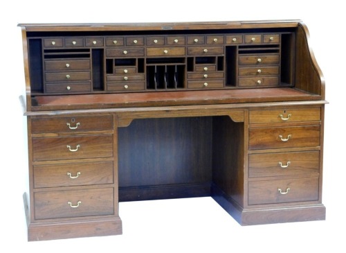 A 20thC oak roll top desk, the tambour front enclosing a dark red leatherette inset with an arrangement of drawers, recesses, etc., the base with a moulded edge above two pedestals each with four drawers, on a plinth base, 127cm high, 183cm wide, 76cm dee