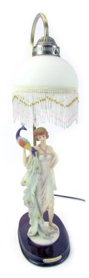 A Juliana Collection table lamp, with frosted glass shade decorated with fringed bead work, above a figure of a lady holding a peacock, on a circular hardwood base, 60cm high.