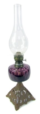 A late 19th/early 20thC oil lamp, with purple glass central reservoir above a pierced cast metal base, with chimney, 53cm high.