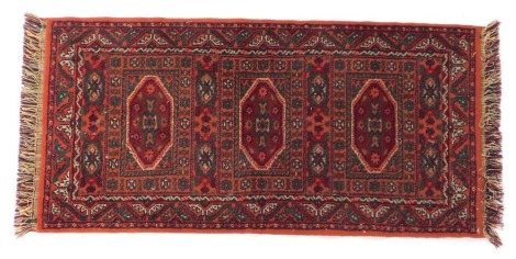 A Persian rug, red ground, decorated centrally with medallions within multiple borders, 140cm x 70cm.