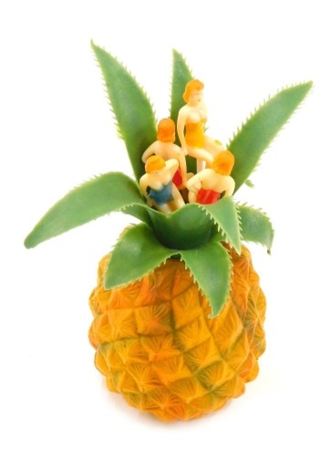 A mid-century novelty plastic cocktail stick holder, modelled in the form of a pineapple, holding four cocktail sticks each with handles modelled as ladies wearing bathing suits, 12cm high.