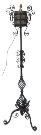 A wrought iron standard lamp, with brass embossed reservoir, the column decorated with scrolls and twisted balusters, the tripod base embellished with leaves, 158cm high.