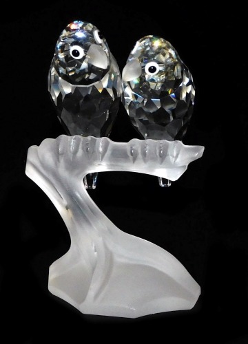 A pair of Swarovski crystal parakeets, modelled perched on the frosted glass branch of a tree stump, 10cm high.