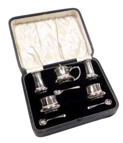 A George V silver five piece condiment set, of outswept, octagonal form, with blue glass liners, comprising; pair of salts and spoons, mustard pot and spoon, and pair of pepperettes, cased, Birmingham 1926, 4.93oz.