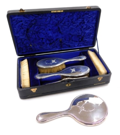 A George V silver backed six piece dressing table set, embossed with a wreath and tied bow, comprising hand mirror, pair of clothes brushes, pair of hair brushes, and a comb, William Hutton & Sons, Birmingham 1916.