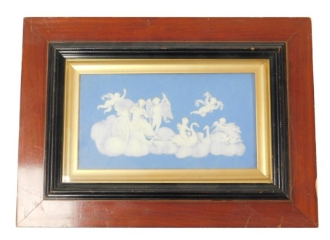 A Wedgwood Jasperware plaque, decorated with Venus in a chariot, on a cloud, drawn by swans and doves, surrounded by Cupid and four putti, within a gilt slip, wooden framed, impressed mark, 11cm high, 20.5cm wide.