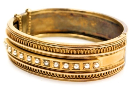 Victorian Etruscan Revival seed pearl set bangle, yellow metal, on a snap clasp, with safety chain as fitted, cased, 28.8g.