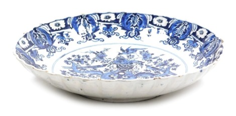 An 18thC Delft blue and white charger, with a wavy border, the centre decorated with a vase surrounded by birds and flowers, within a repeating floral border, unmarked, 34.5cm diameter.