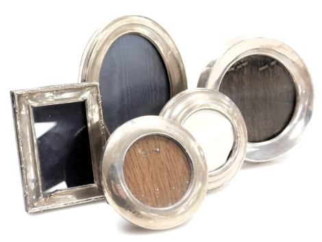 A group of small silver strut photograph frames, three circular, one oval, and one rectangular. (5)