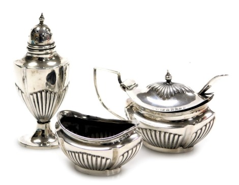 An Edward VII/George V silver three piece condiment set, of semi fluted form, comprising salt, pepperette, and mustard pot, with unmatched spoon, Birmingham 1909/1911, 3.39oz.