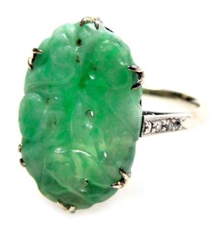 A jade ring, of oval carved sinuous form, in a claw setting, with diamond set shoulders, white metal, stamped 18 and Pt, size N, 5.3g.