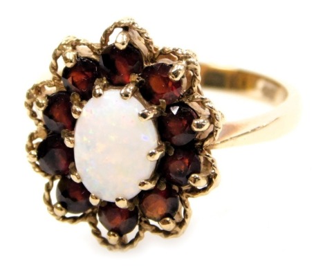 An opal and garnet ring, the oval cabachon opal in a surround of brilliant garnets, within a claw setting, in yellow metal, stamped 9ct, size P, 4.0g.