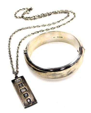 A silver bangle, with engraved foliate decoration, on a snap clasp, with safety chain as fitted, together with a silver ingot pendant on chain, 55.1g.