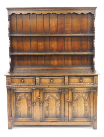 An Old Charm oak dresser, the plate rack with an outswept pediment over two shelves, above three frieze drawers, over three carved panelled doors, raised on stiles, 179.5cm high, 138cm wide, 47cm deep.