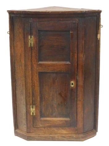 An early 19thC oak wall hanging corner cupboard, with a single double panelled door enclosing three shaped shelves raised on a plinth base, 109cm high, 76cm wide, 43.5cm deep.