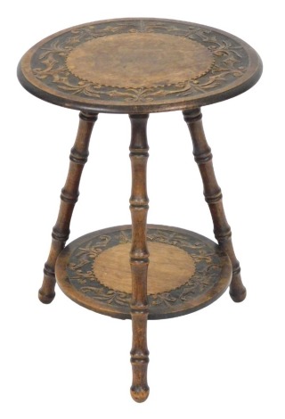 A Victorian Arts & Crafts mahogany two tier occasional table, with a circular top carved with repeating fleur de lis, raised on three faux bamboo legs, 50cm high, 37.5cm diameter.