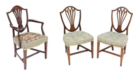 A pair of George III mahogany shield back single dining chairs, upholstered in patterned green fabric, together with a shield back carver chair, with a wool work seat. (3)