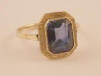A dress ring set with a trap cut sapphire of 9.8mm x 7.6mm set in a simple rub over mount