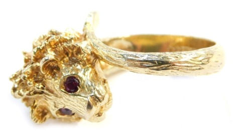 A 9ct gold dress ring, in the form of a cast lion's head with ruby eyes, the shank formed by a tail, size R 1/2, 15.3g all in.