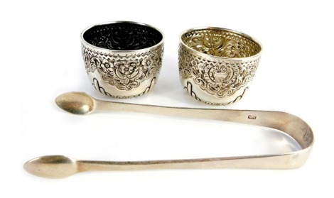 A pair of Victorian silver open salts, each of circular form embossed with part fluted decoration, scrolls, etc., Vale Brothers and Sermon, London 1893, together with a pair of Georgian sugar tongs, 2.96oz.