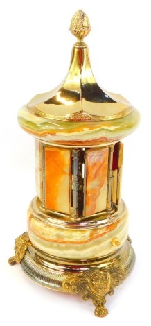 A 20thC onyx and brass carousel cigarette dispenser, with six hinged doors, enclosing a recess for cigarettes, with a model of a peacock to the centre, on an ornate brass base, raised on three paw feet, 42cm high.