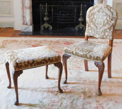 A walnut side chair in the Queen Anne style, with padded back, the seat upholstered in brown and beige patterned fabric, on carved cabriole legs with scroll carved pad feet, together with a similar stool. The upholstery in this lot does not comply with th