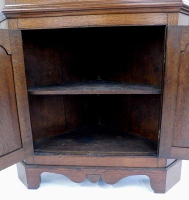 A late 18thC George III oak and mahogany corner display corner, with an out swept pediment, over an astragal glazed door, enclosing a cream painted interior with three shelves, above a pair of cupboard doors, enclosing a further shelf, raised on bracket f - 2