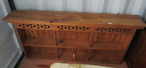 A pine hanging wall shelf, the moulded top above a pierced section, the base with two shelves supported by turned columns, 84cm high, 172cm wide, 26.5cm deep.