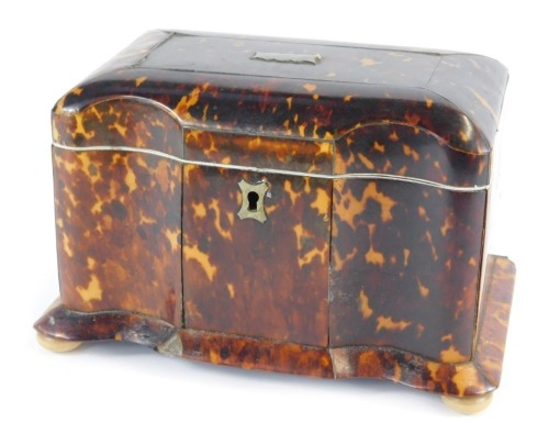 A Georgian tortoiseshell serpentine tea caddy, with silver and ivory inlay, the hinged lid opening to reveal two lidded compartments, raised on bun feet, 20cm wide.