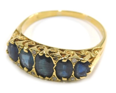 An 18ct gold sapphire and diamond half hoop dress ring, set with five oval sapphires each in claw setting with tiny diamonds, scroll design shoulders, ring size T½, 5.5g all in.