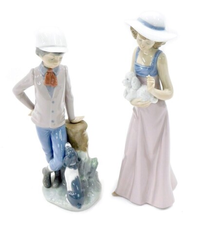 Two Nao porcelain figures, modelled as lady holding dog, and young boy leaning against tree stump beside dog.