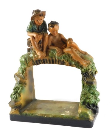 An early 20thC Chalkware centrepiece, modelled in the form of two boys seated above an arched alcove, 40cm wide.