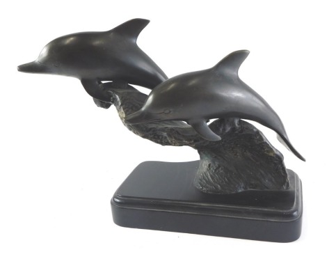 A cast bronze sculpture of two dolphins on a wave, on a rectangular plinth, unsigned, 30cm high.