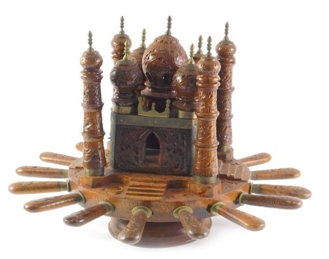 An early to mid 20thC Indian teak cutlery set, of wheel form, the top decorated with a temple, possibly the Taj Mahal embellished in brass, surrounded by knives and two pronged forks, each numbered, 45cm diameter.